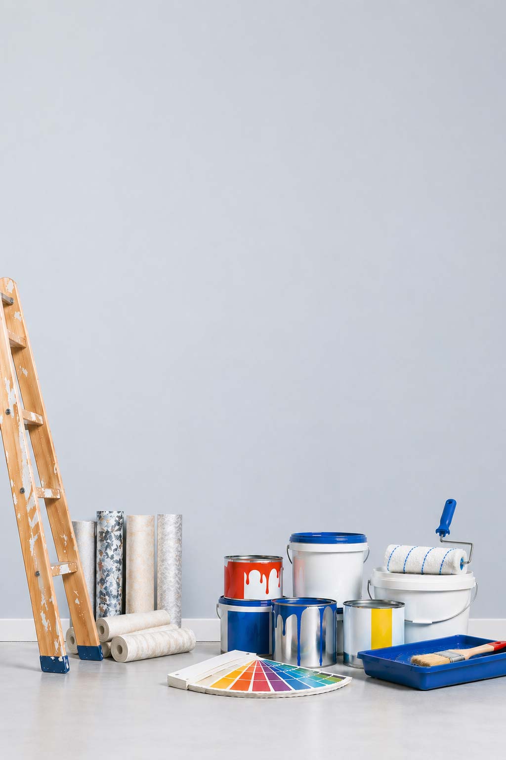 Farbeimer, Farbroller, Pinsel, Leiter, Tapetenrollen vor einer Wand